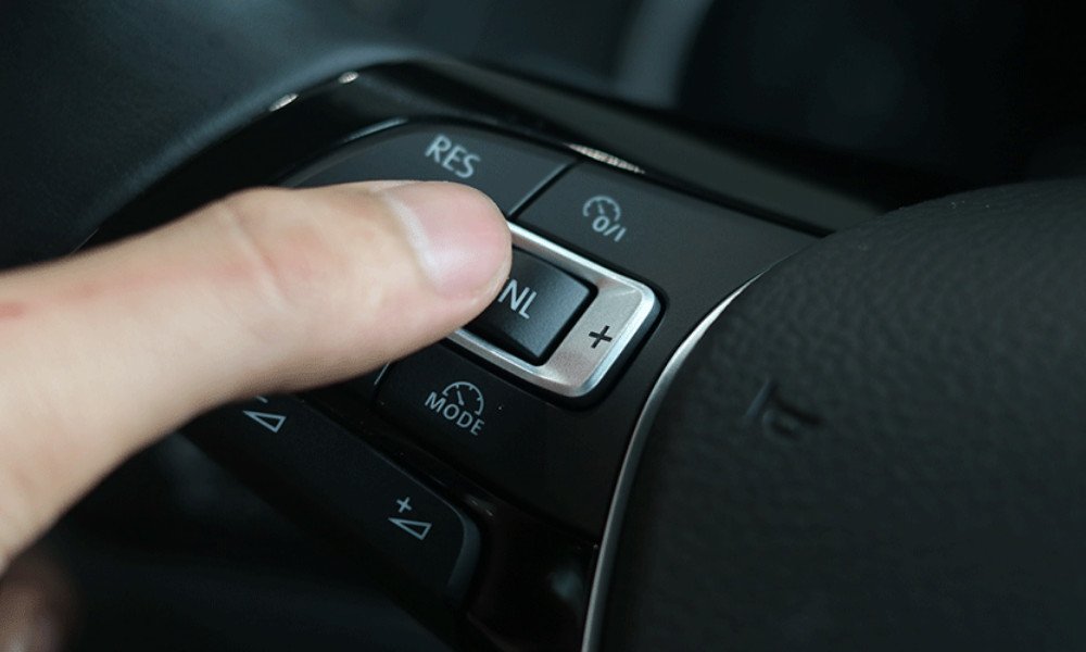Cận cảnh tay người lái bấm nút kích hoạt Cruise Control trên vô lăng.